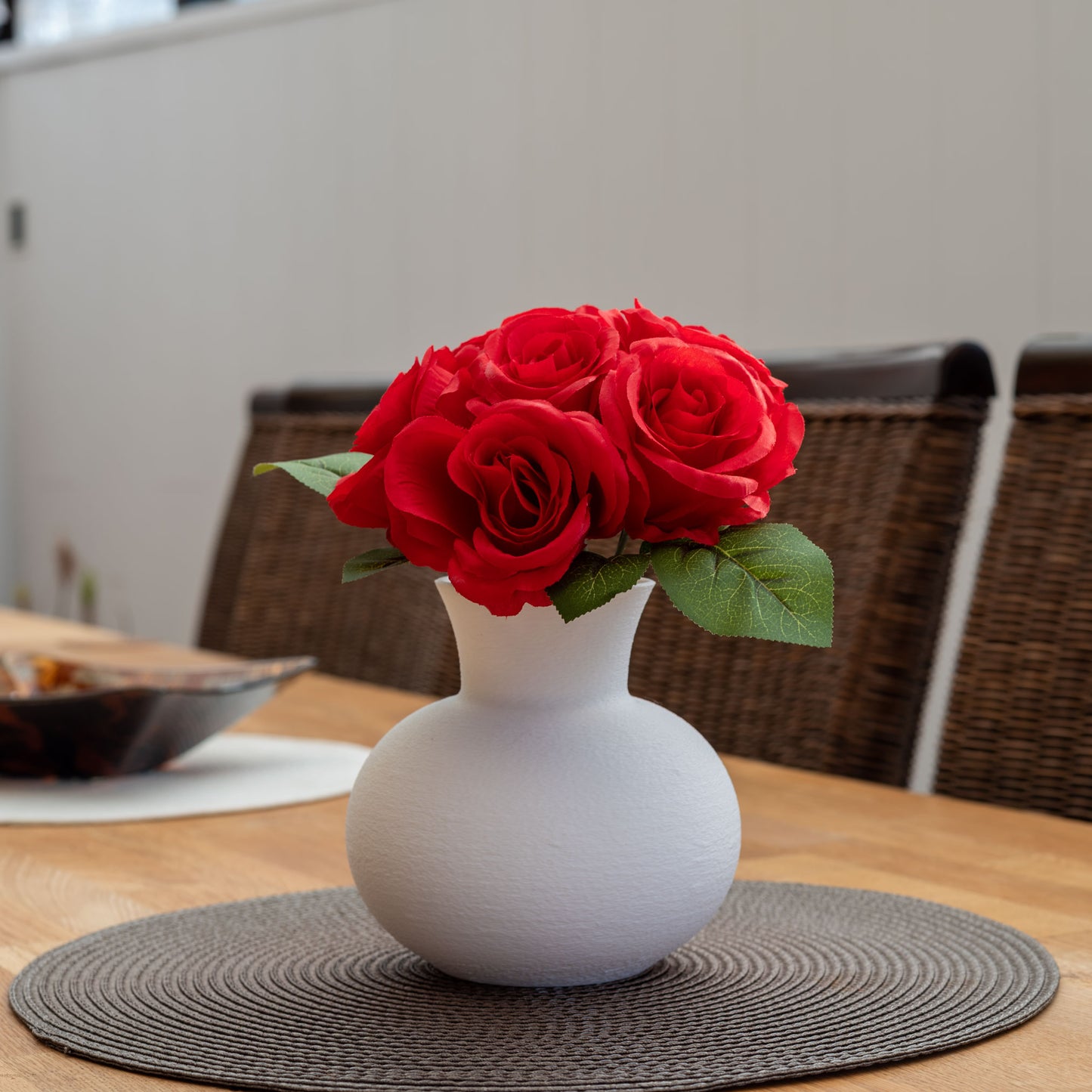 Weiße, nachhaltige Vase aus PLA mit matter, leicht strukturierter Oberfläche, dekorativ arrangiert mit einem Strauß roter Rosen auf einem gedeckten Holztisch – stilvoll und umweltfreundlich.