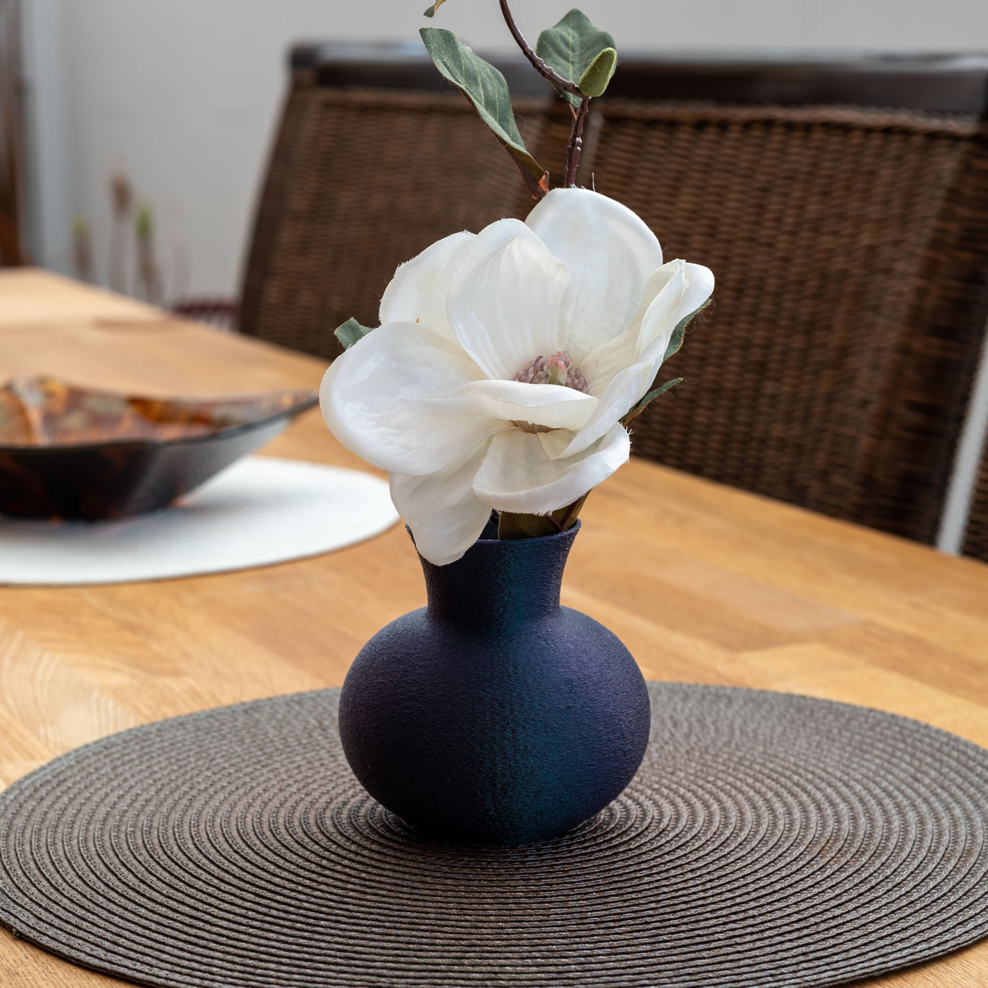 changierendem Dunkelblaue nachhaltige Vase aus PLA mit matter, leicht strukturierter Oberfläche, dekorativ arrangiert mit einem Blume auf einem Esstisch – stilvoll und umweltfreundlich.