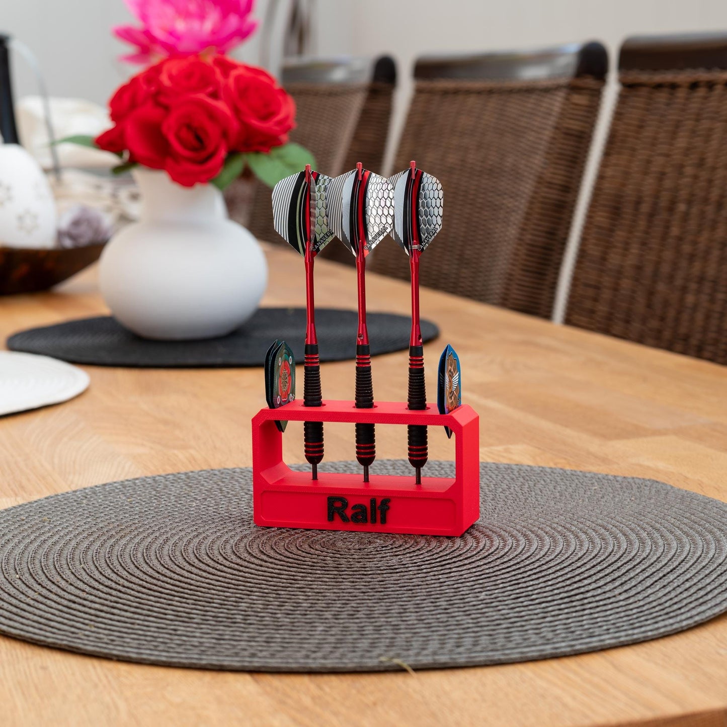 Roter 3D-gedruckter Darthalter aus nachhaltigem PLA mit dem Namen 'Ralf', hält drei Darts mit silbernen Flights auf einem Holztisch