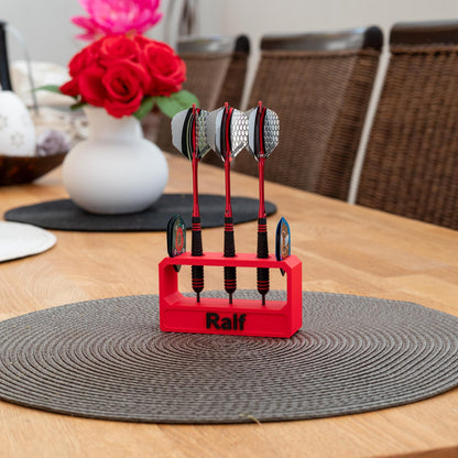 Roter 3D-gedruckter Darthalter aus nachhaltigem PLA mit dem Namen 'Ralf', hält drei Darts mit silbernen Flights auf einem Holztisch