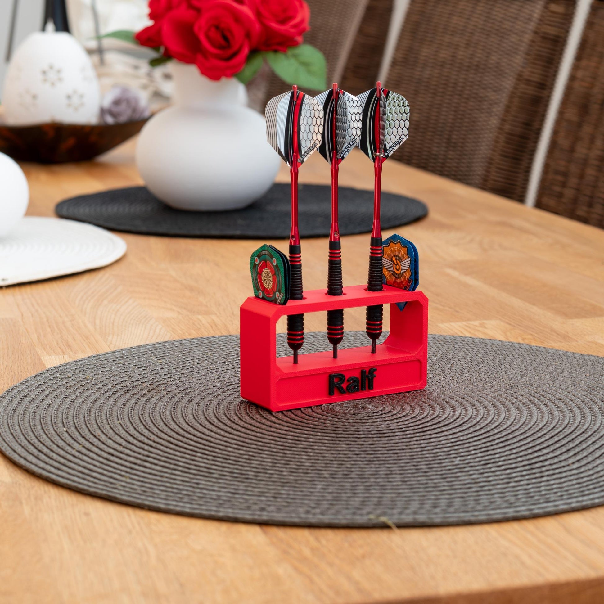 Roter 3D-gedruckter nachhaltiger Darthalter aus PLA mit drei Darts und dem Namen 'Ralf' auf einem Holztisch