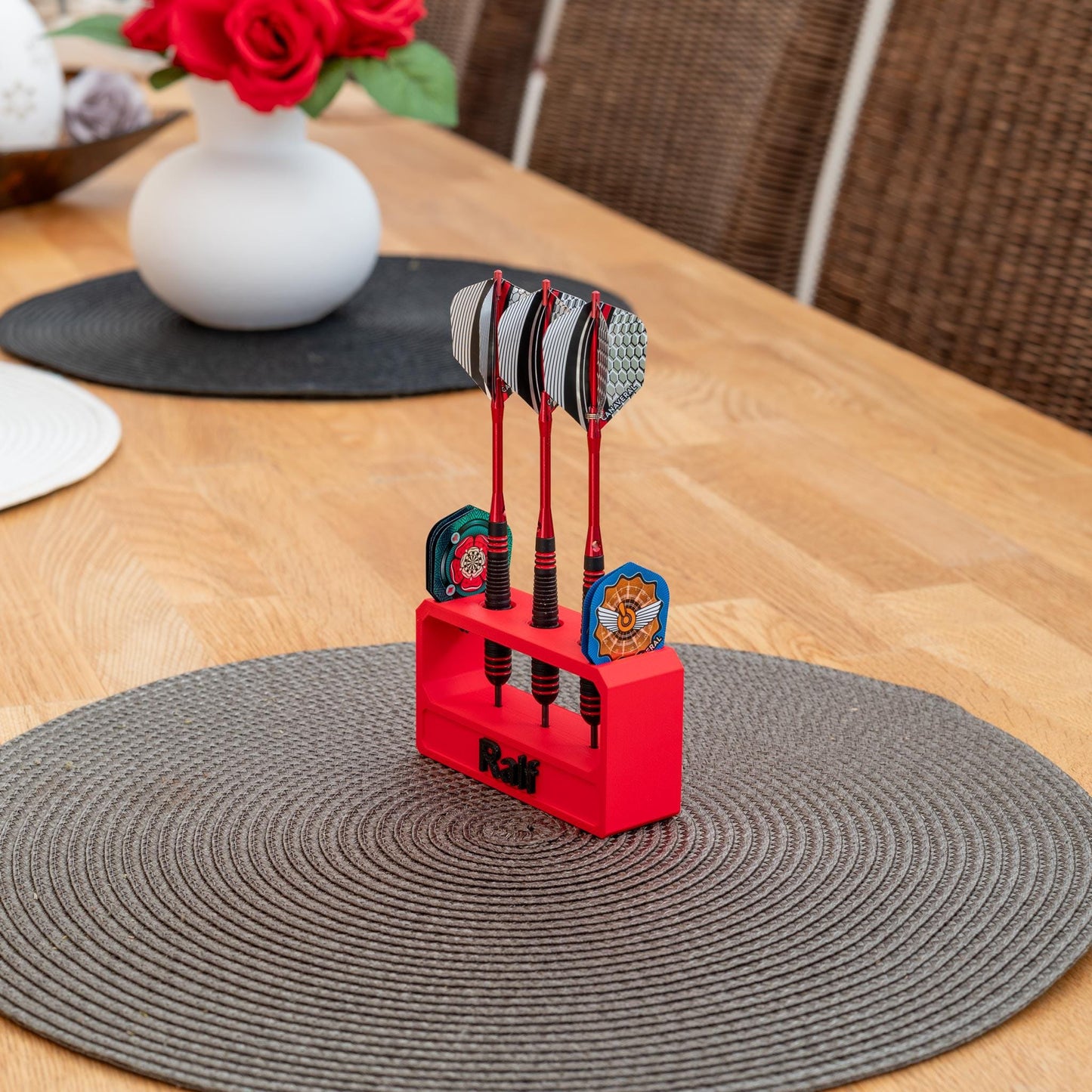 Roter 3D-gedruckter Dart- und Flightshalter aus nachhaltigem PLA mit drei Darts auf einem braunen Tischset