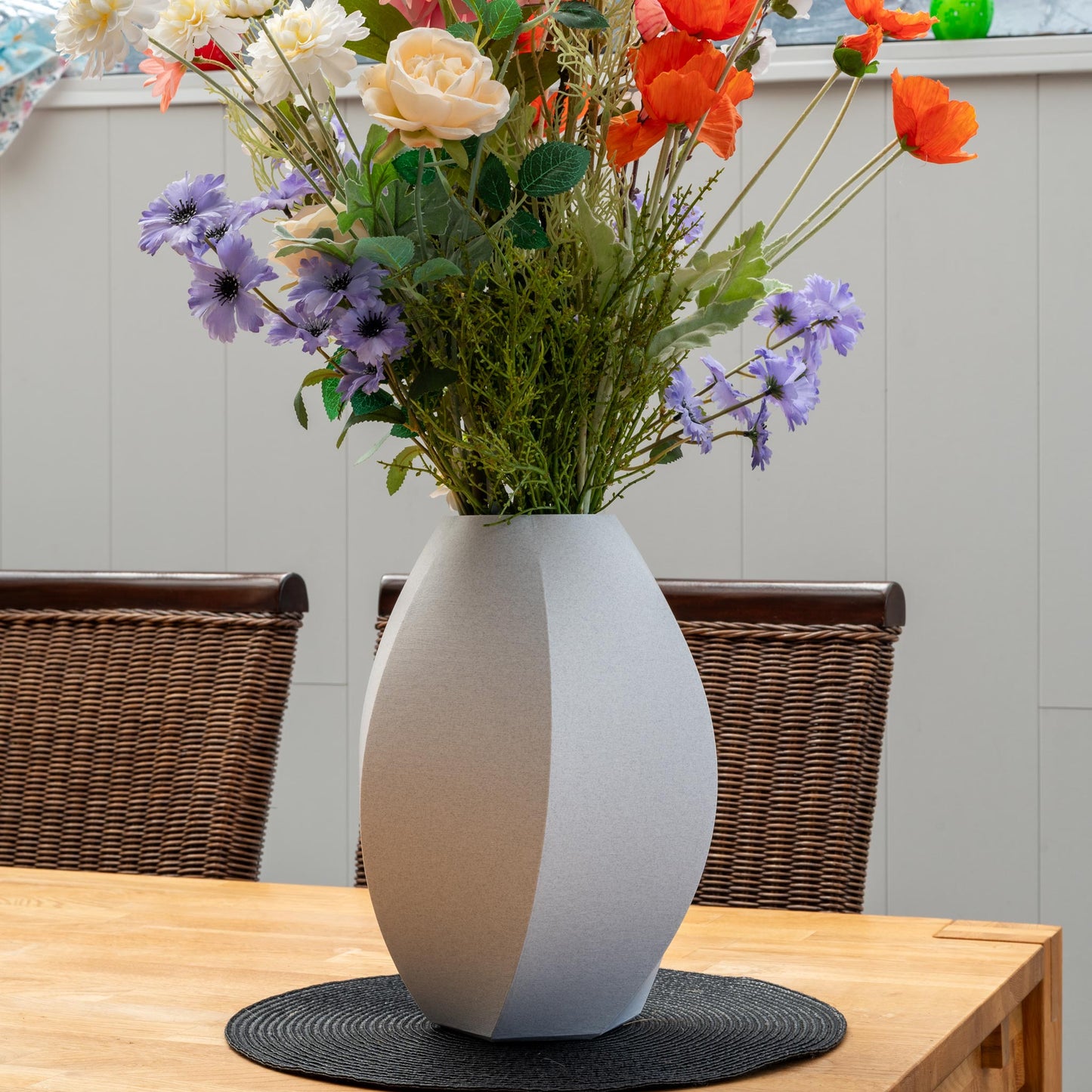 Sechseck-Vase aus PLA in der Farbe Schattensturm Marmor, gefüllt mit bunten Kunstblumen, auf einem Esstisch mit dunklem Platzset – nachhaltig und dekorativ.