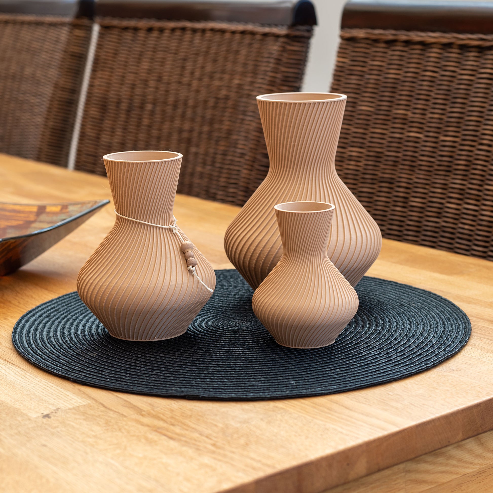 Drei nachhaltige Vasen aus PLA in verschiedenen Größen mit gerillter Oberfläche, 3D-gedruckt, auf einem schwarzen runden Tischset