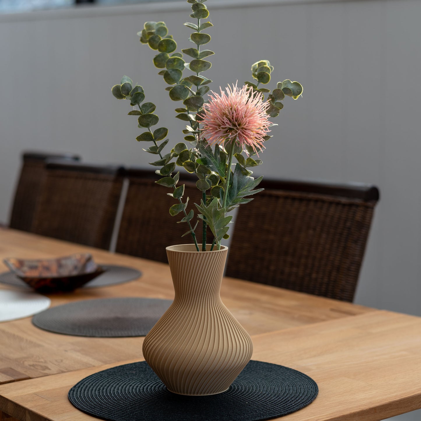 Nachhaltige Vase Line aus PLA im 3D-Druck, beige, mit gerillter Oberfläche, gefüllt mit Eukalyptuszweigen und einer rosa Blume auf einem Holztisch