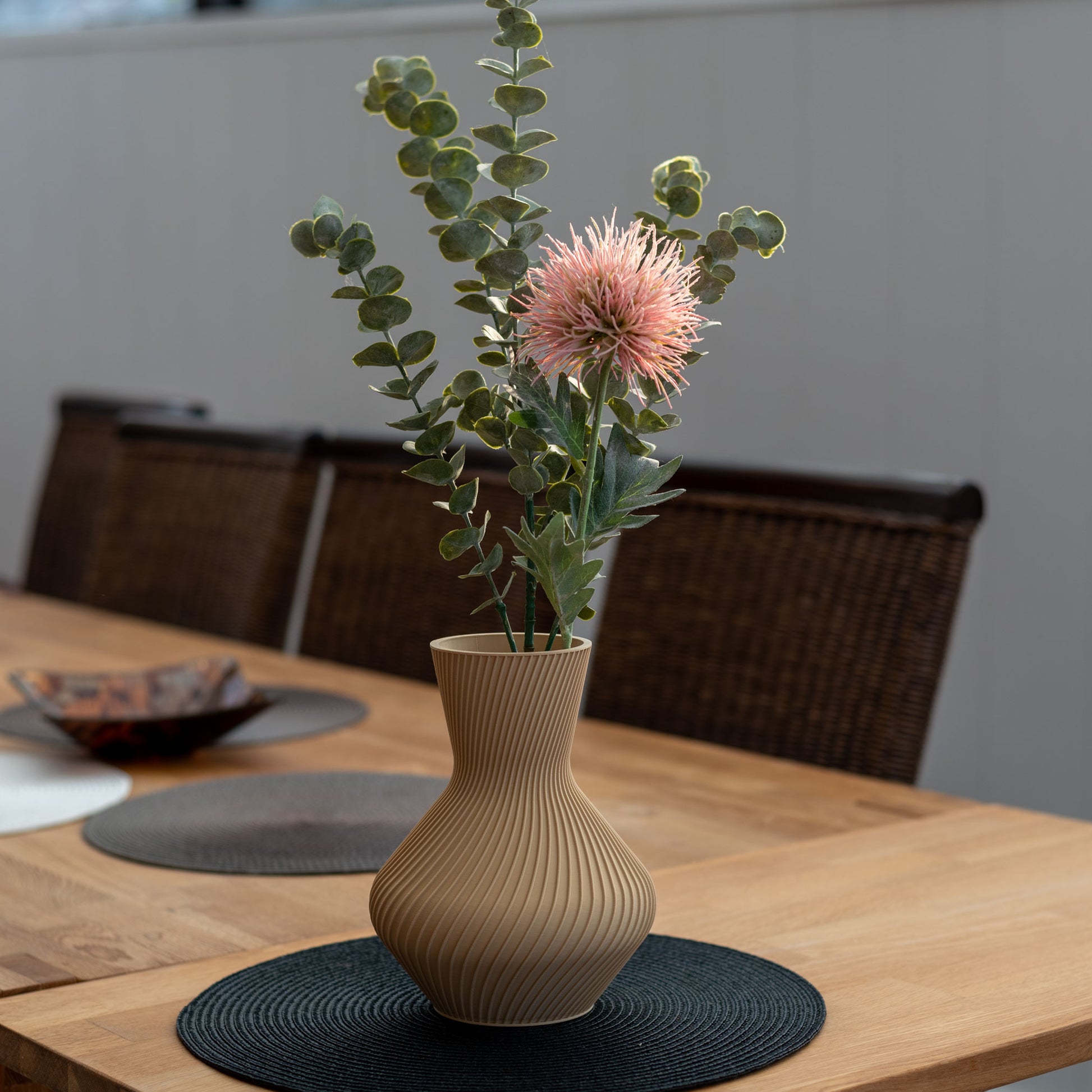 Nachhaltige Vase Line aus PLA im 3D-Druck, beige, mit gerillter Oberfläche, gefüllt mit Eukalyptuszweigen und einer rosa Blume auf einem Holztisch