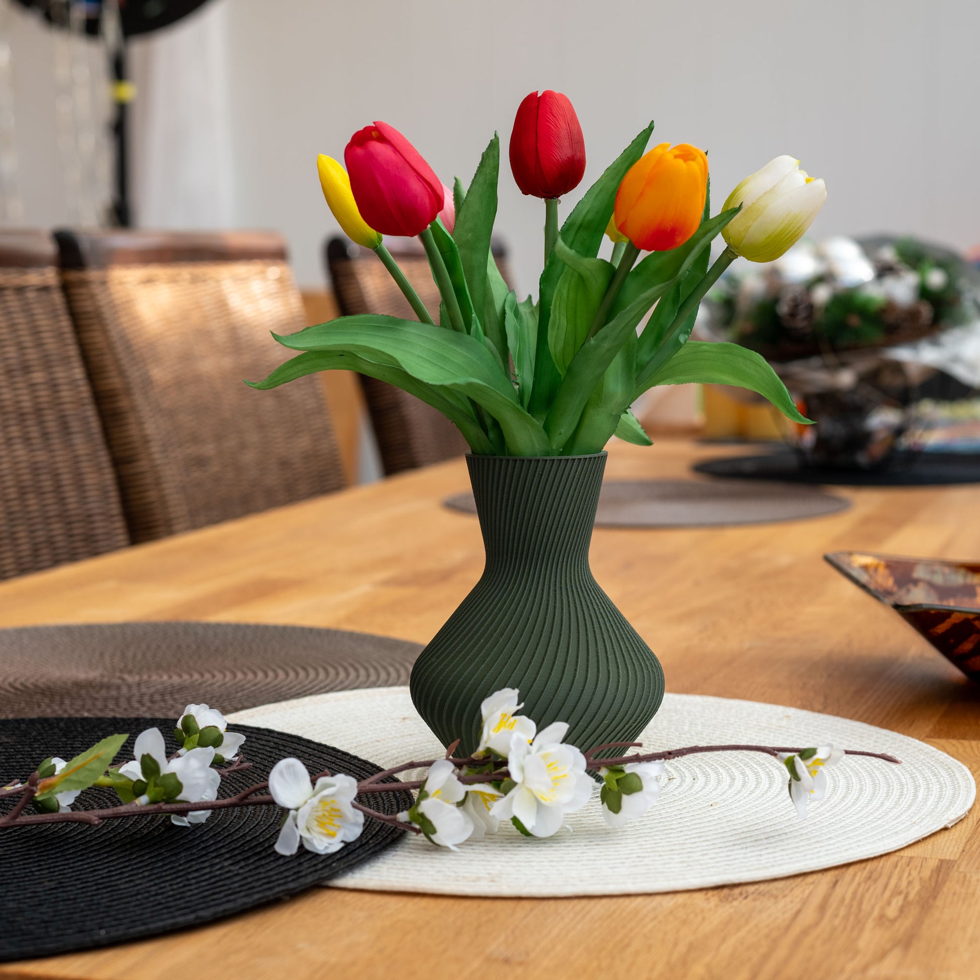Nachhaltige Vase Line aus grünem PLA mit gerillter Oberfläche, 3D-gedruckt, gefüllt mit bunten Tulpen auf einem Tisch