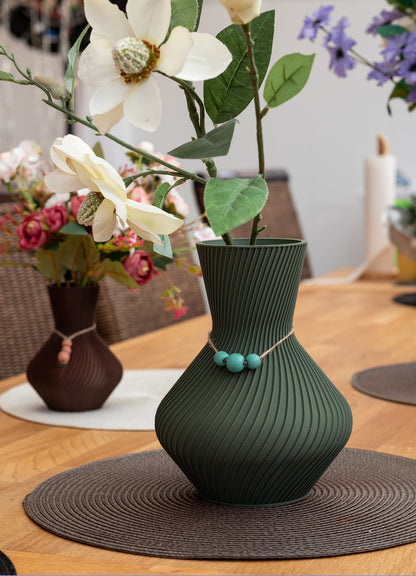 Grüne Vase Line aus nachhaltigem PLA mit geripptem Design, 3D-gedruckt, mit weißen und grünen künstlichen Blumen auf einem Tisch