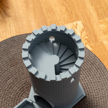 Runder grauer Würfelturm mit Zinnen und einer spiralförmigen Treppe im Inneren, auf einem Holzboden und einem braunen Teppich