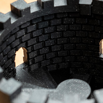 Detailaufnahme eines schwarzen, glitzernden Würfelturms aus nachhaltigem PLA 3D-Druck mit Zinnen und gemauertem Innenmuster